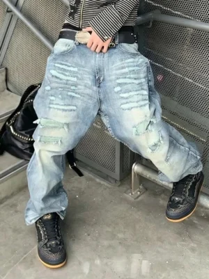Model wearing black dragon-scale streetwear sneakers with distressed baggy jeans in an industrial concrete stairwell