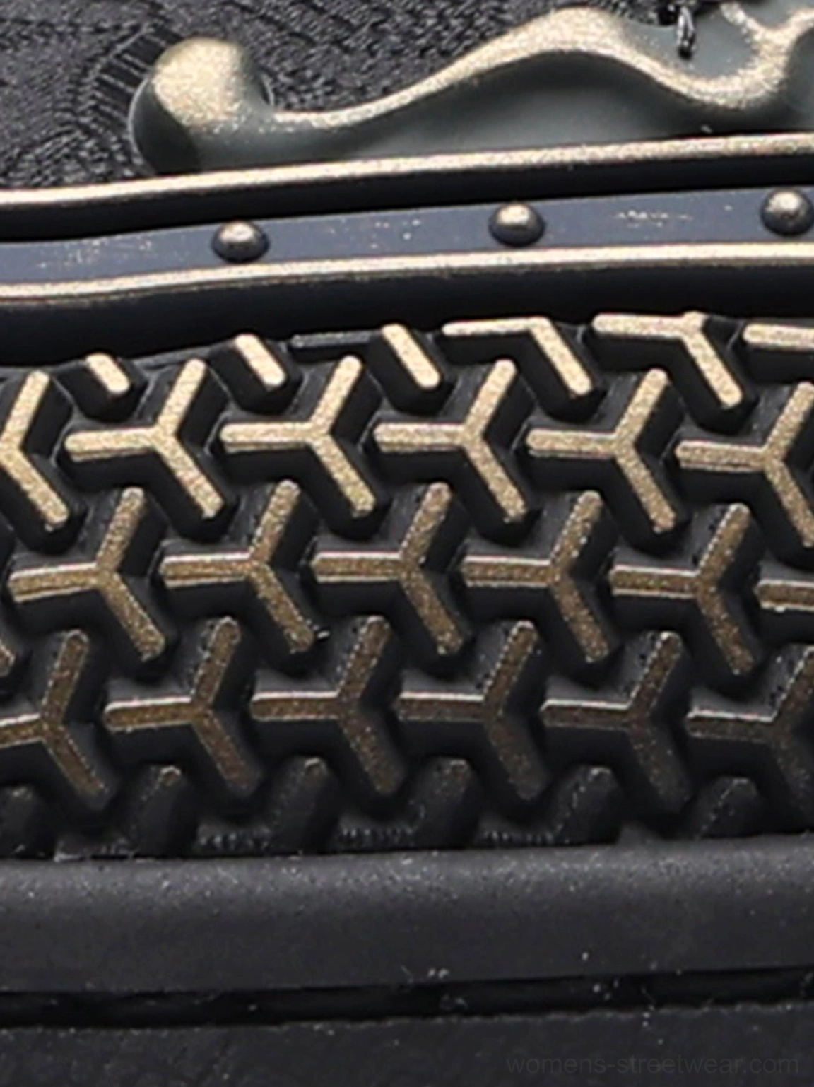 Close-up side view of black dragon sneaker upper with bronze ornament, metal rivets, red strap, and geometric perforations