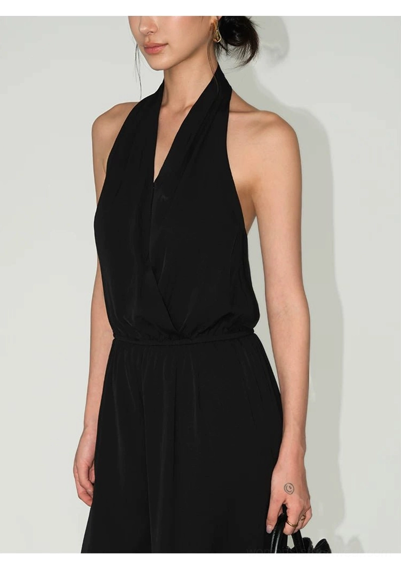 Close-up front view of black draped halter wide-leg jumpsuit styled with a handbag