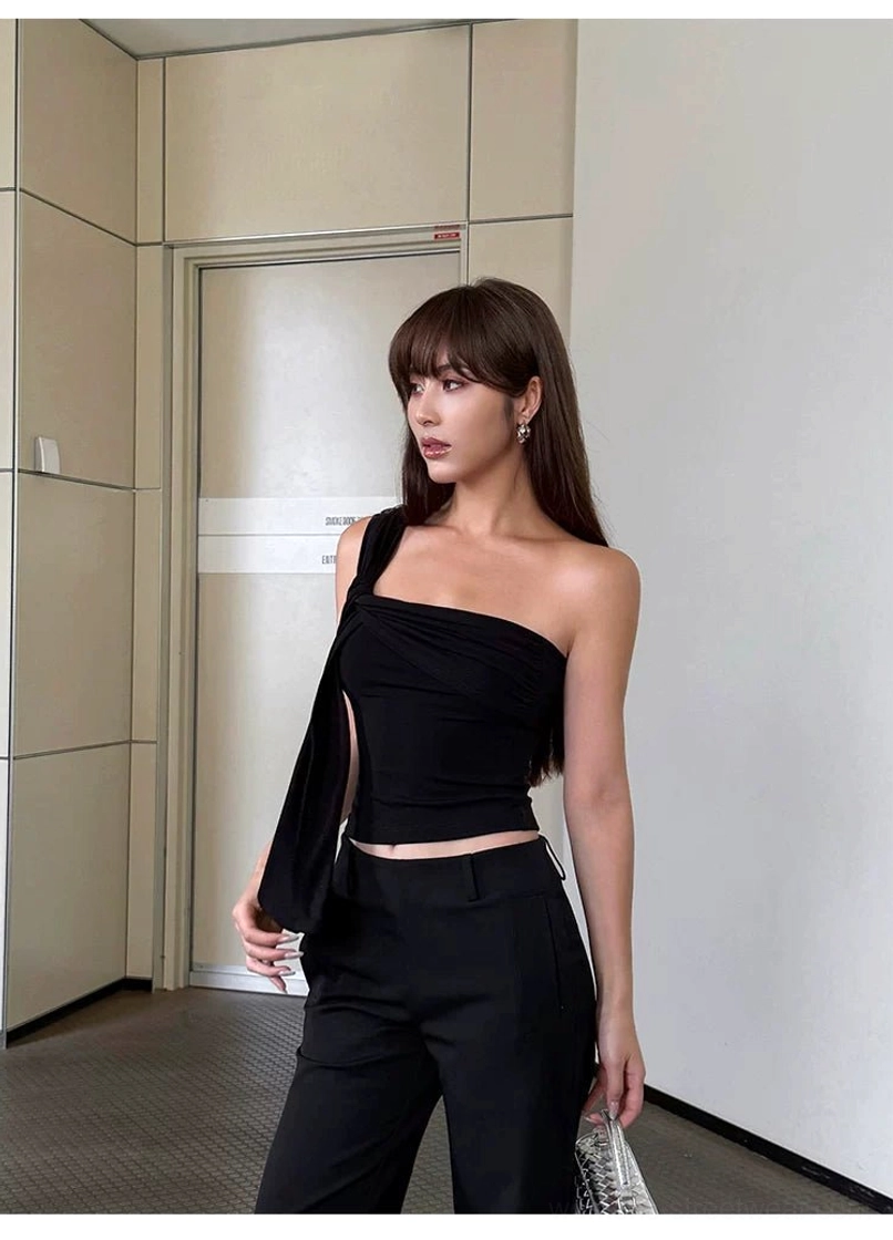 Black draped one-shoulder crop top with sash falling toward the hip styled with wide-leg trousers