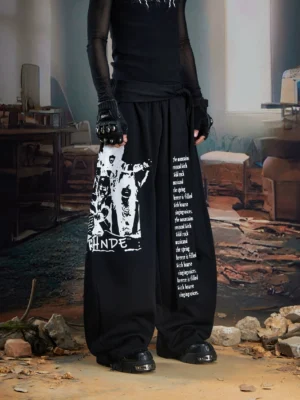Black draped panel graphic wide-leg streetwear joggers styled with sheer black top and platform boots front full-body view