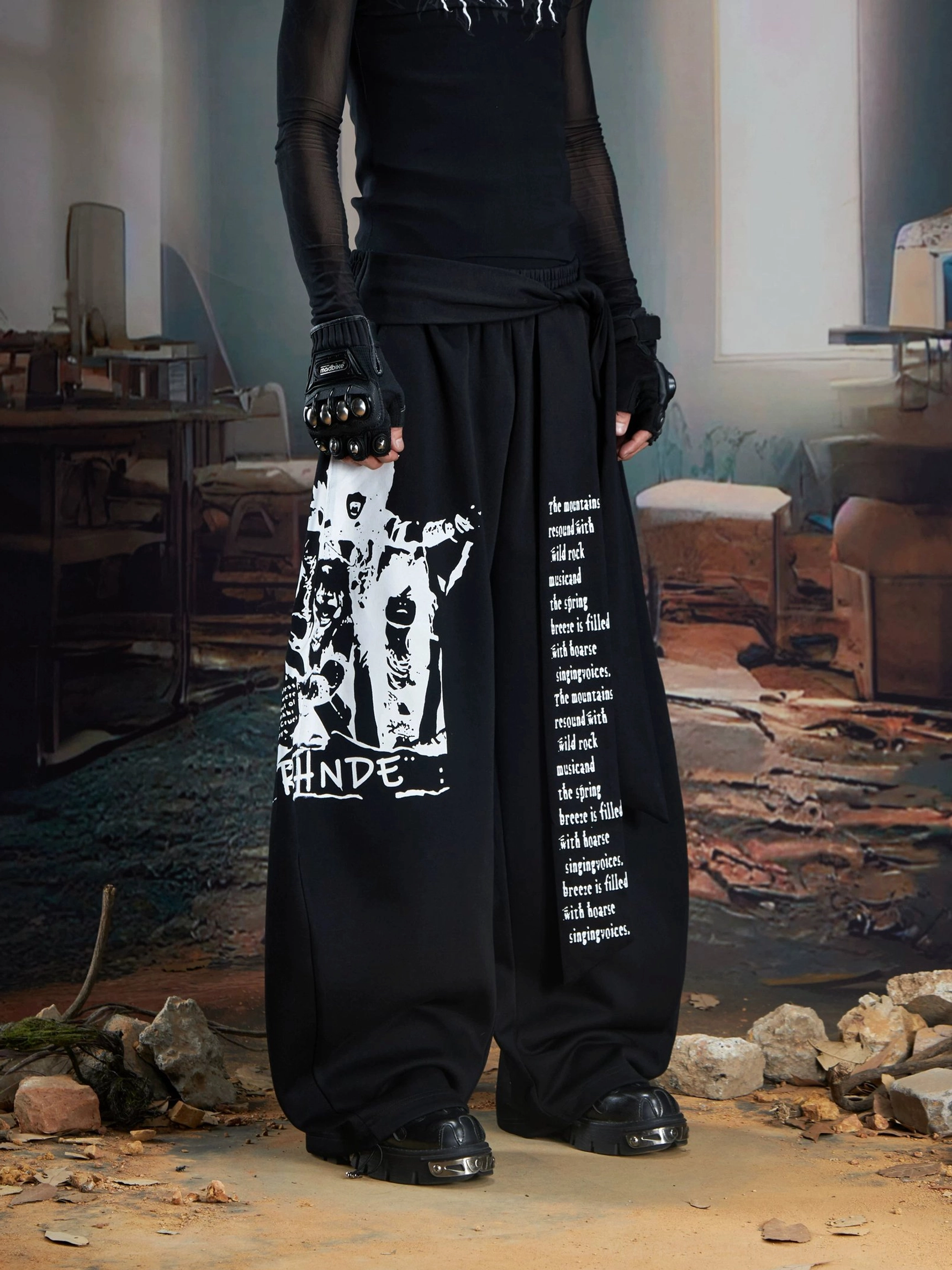 Black draped panel graphic wide-leg streetwear joggers styled with sheer black top and platform boots front full-body view