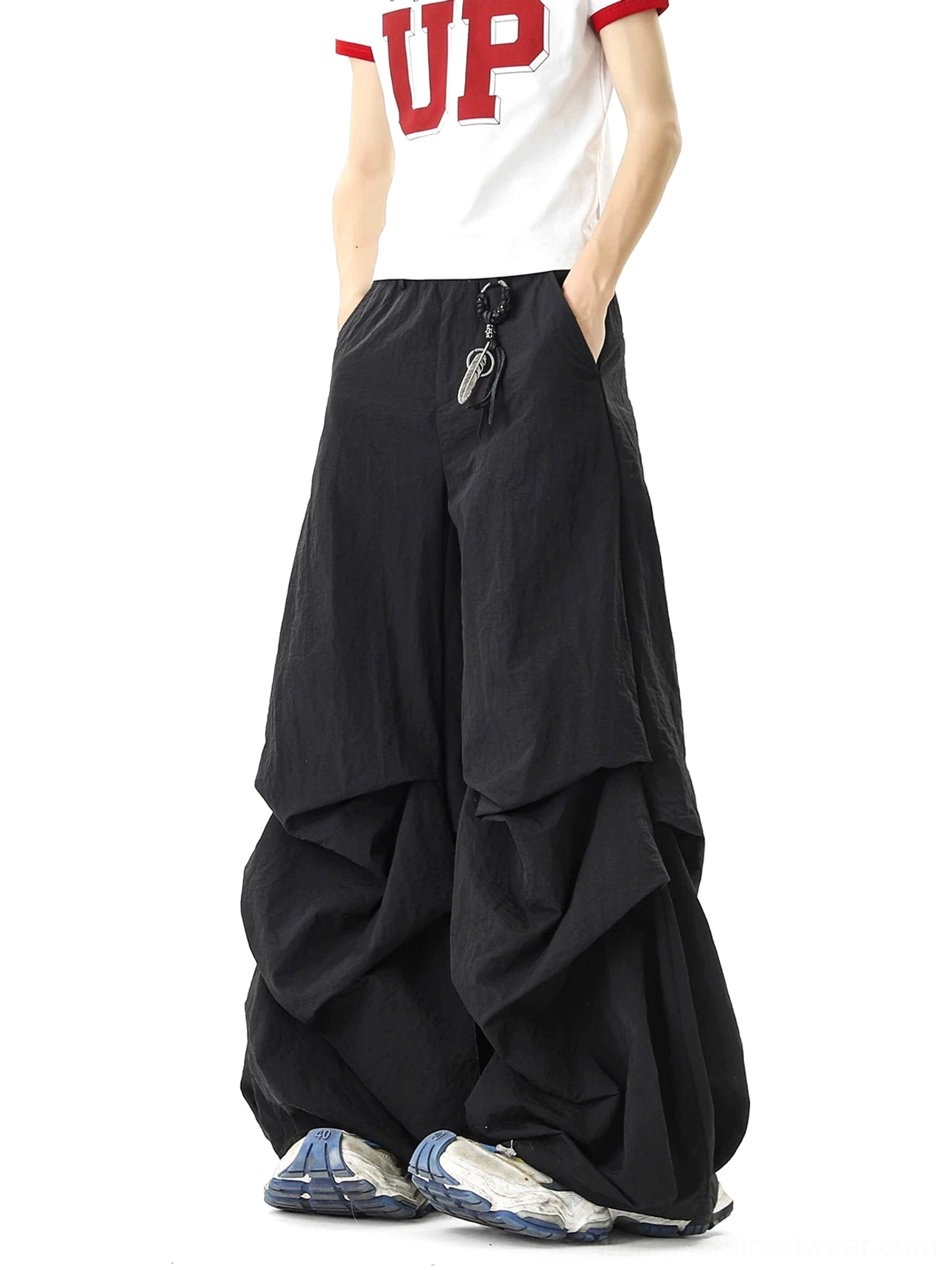 Front view of black draped parachute pants with pleated wide legs, waist-mounted key ring accessory, cropped graphic tee, and casual streetwear sneakers