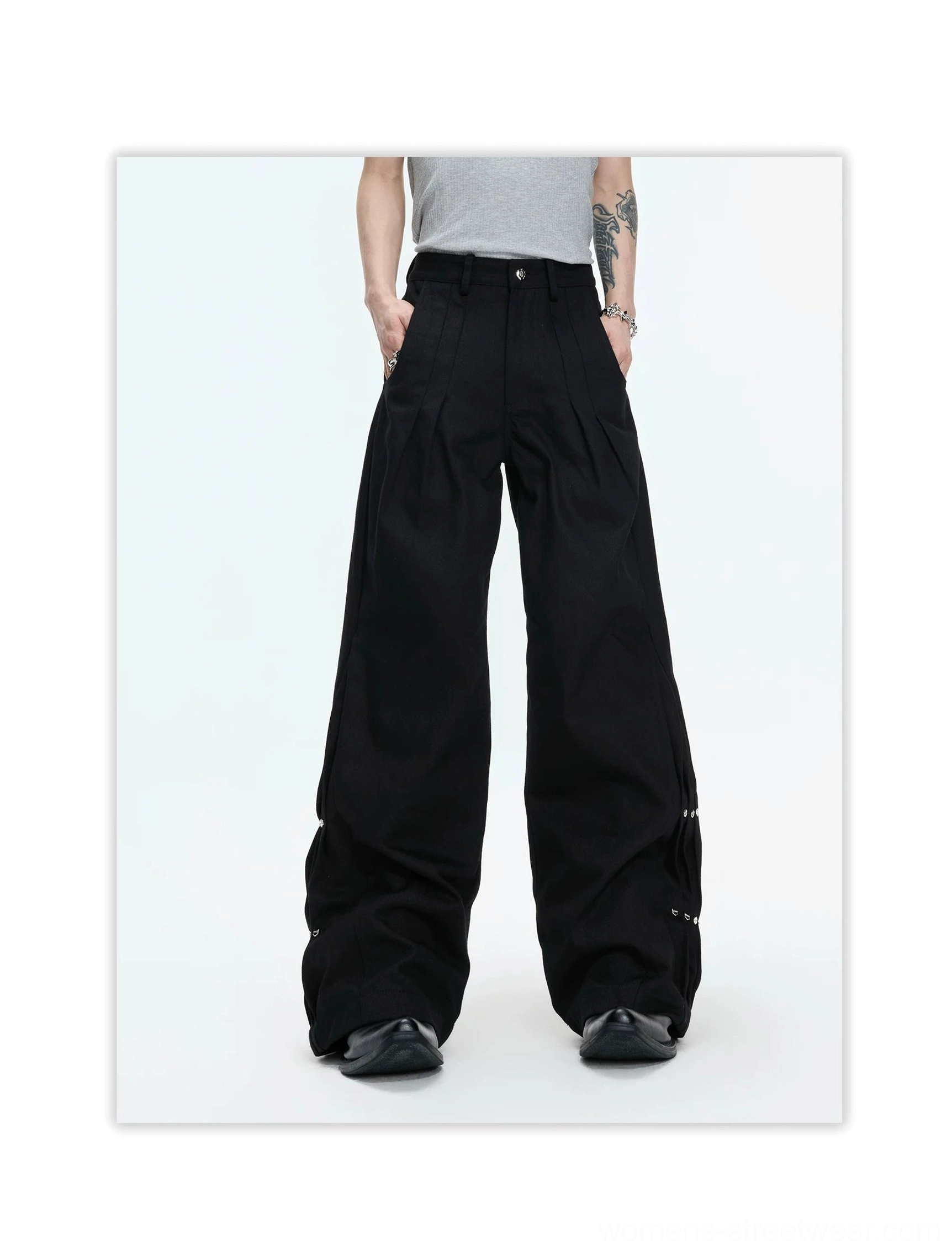 Back view of black draped wide-leg streetwear trousers featuring a relaxed oversized cut, rear pockets, and metal rivet accents near the lower leg openings