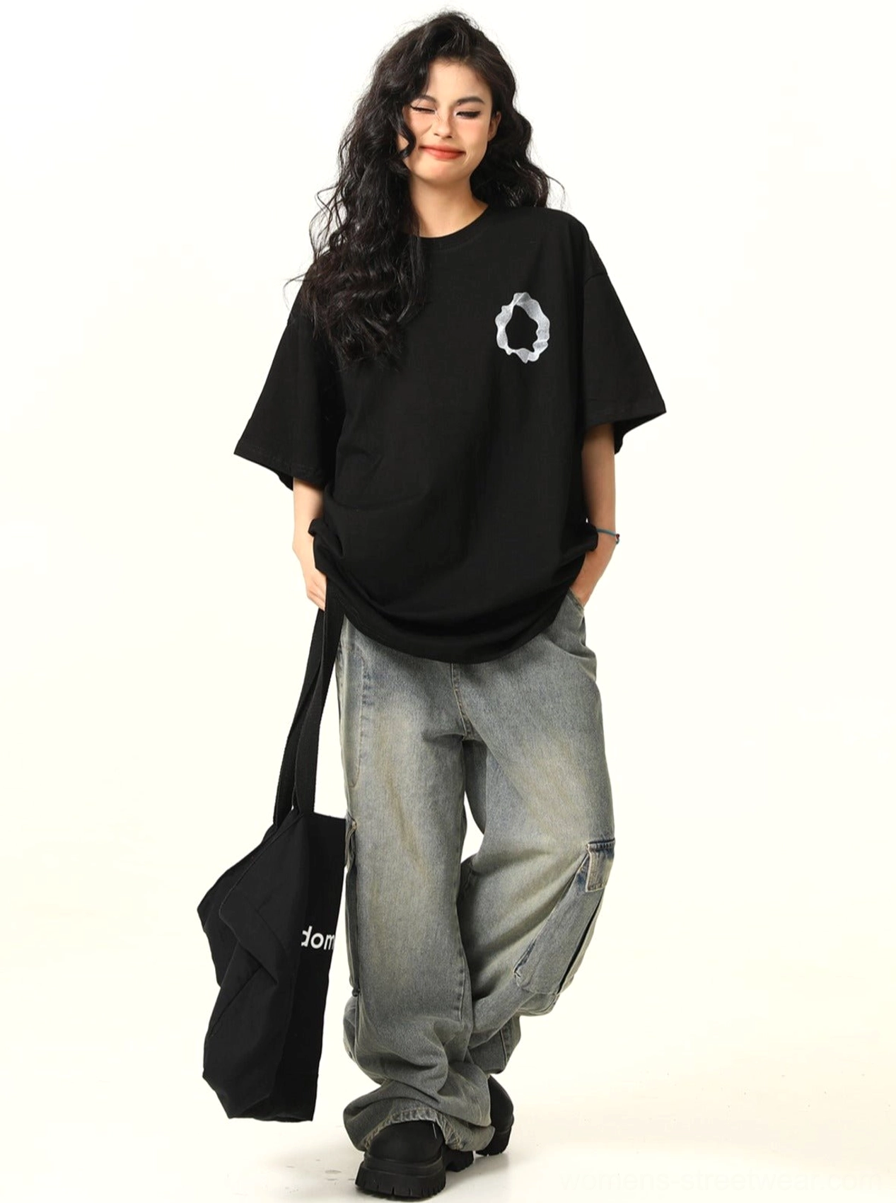Walking front view of black drop shoulder oversized cotton tee with abstract white chest graphic and curved hem