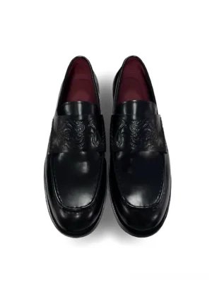 Black embossed leather loafers shown from a top-down front view with glossy polished leather, square toes, burgundy red lining, and patterned vamp detail