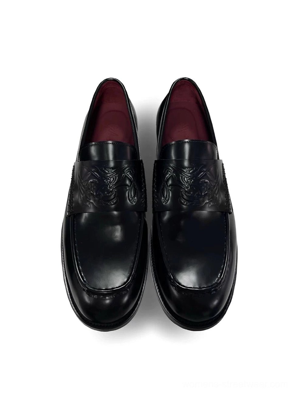 Black embossed leather loafers shown from a top-down front view with glossy polished leather, square toes, burgundy red lining, and patterned vamp detail