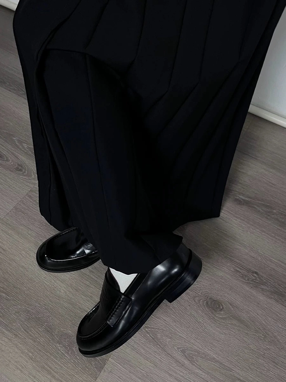 Black embossed leather loafers worn with tailored black trousers on a wooden floor for a refined streetwear and formal outfit