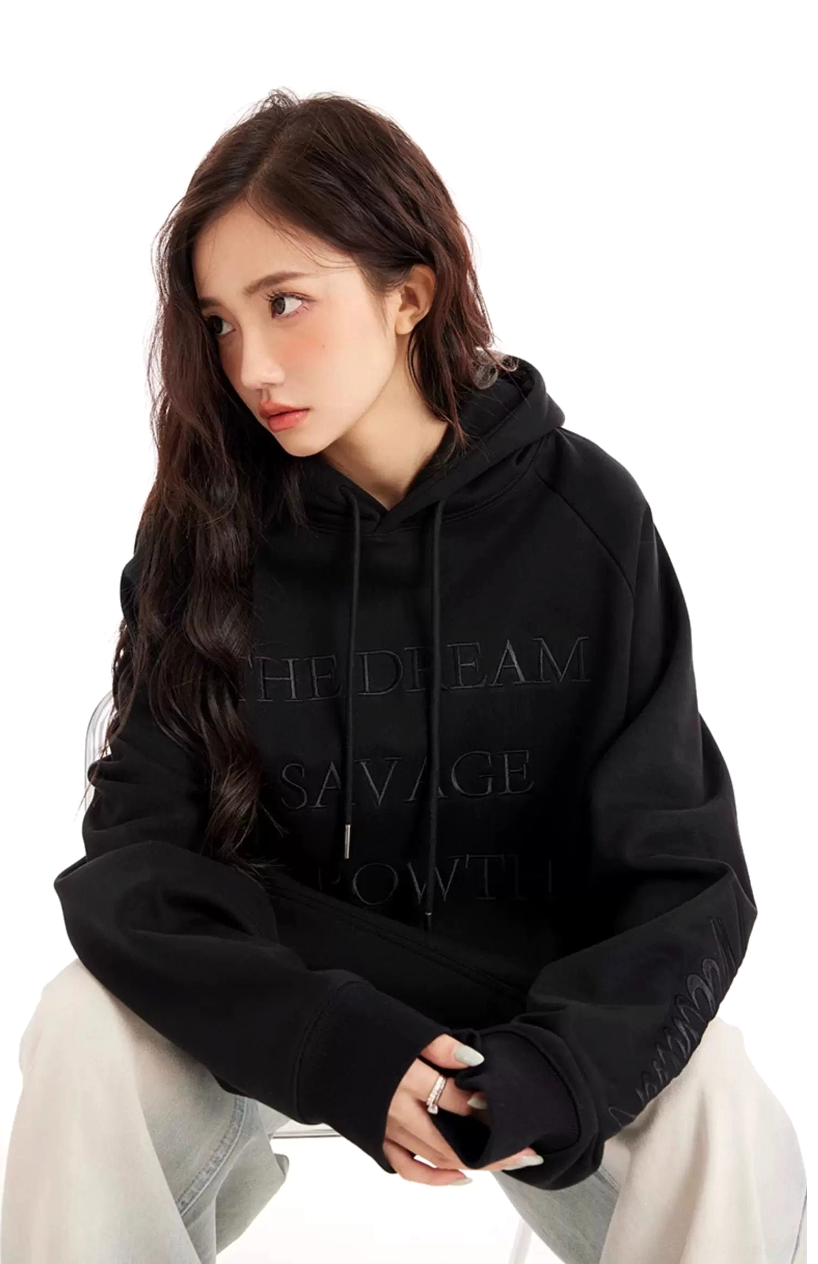 Black embossed lettering streetwear hoodie shown in a low-angle relaxed pose with kangaroo pocket and adjustable hood