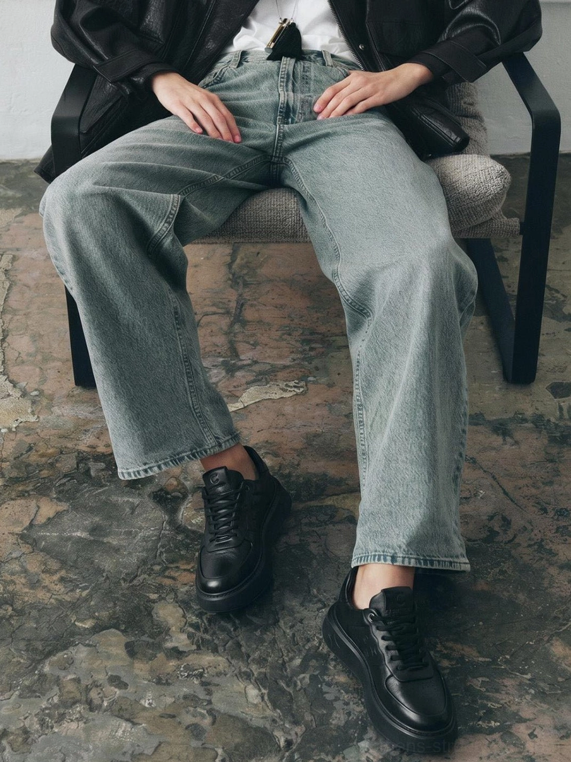 Black embossed platform low-top sneakers worn with light wash jeans in a seated streetwear outfit