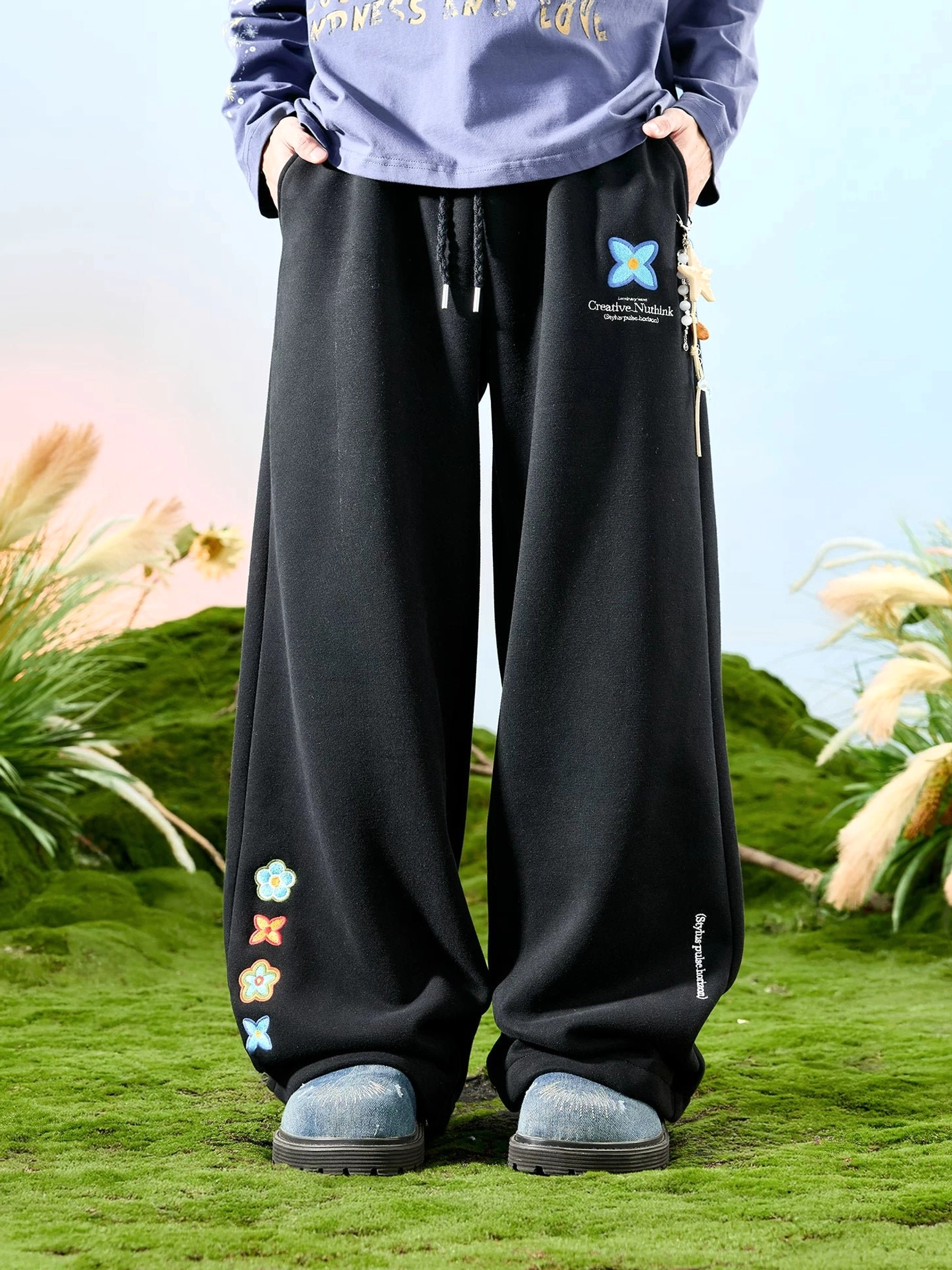 Black embroidered floral drawstring wide-leg sweatpants showing colorful cuff embroidery and relaxed straight leg fit