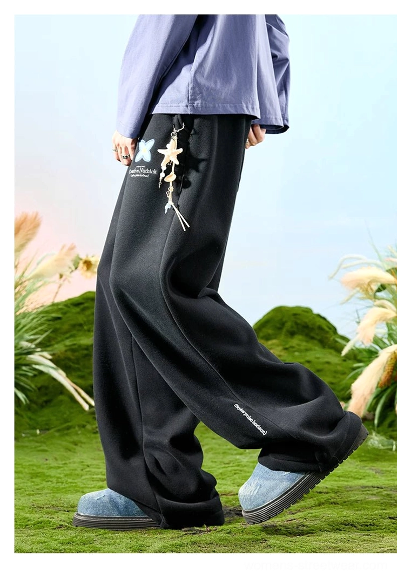 Black embroidered floral wide-leg streetwear sweatpants with hanging starfish ornament shown in a side movement view