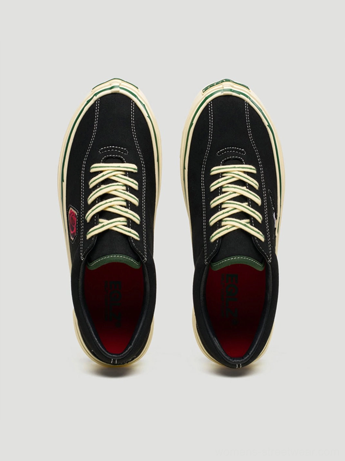 Top-down flat lay of matching black embroidered low-top skate shoes with beige laces, dark red lining, and green collar trim