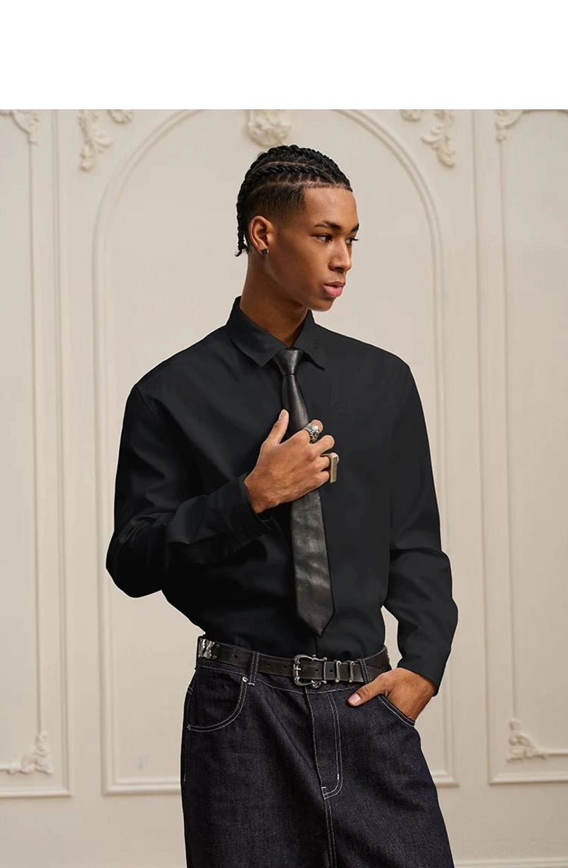 Model adjusting a necktie while wearing a black embroidered long-sleeve shirt with dark jeans and leather belt