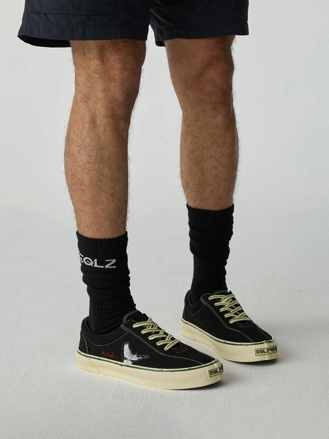 Black embroidered skate shoes styled on feet with casual shorts, dark socks, and a neutral streetwear outfit