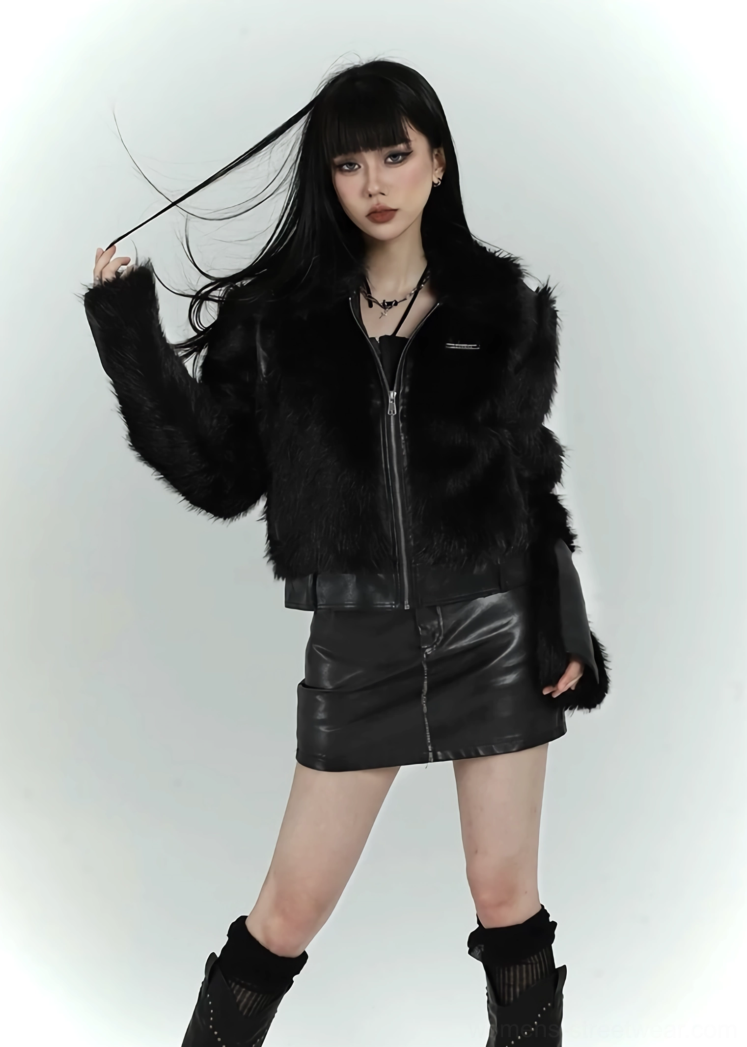 Front three-quarter view of a woman wearing a black faux fur cropped bomber jacket with a front zipper and dark goth streetwear styling