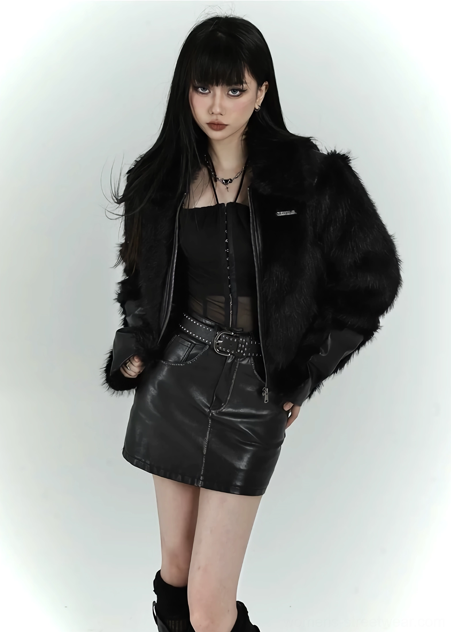 Woman wearing a black faux fur cropped bomber jacket with layered dark tops and a belted skirt in an alternative streetwear look