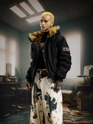 Male model wearing a black padded hooded bomber jacket with brown faux fur trim and wide-leg cow print pants