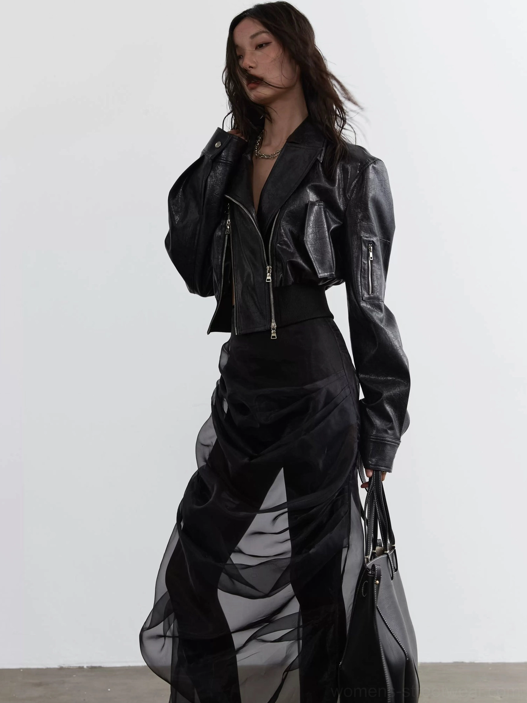 Side view of a black faux leather cropped biker jacket featuring classic notched lapels, asymmetrical front zipper, glossy texture, and edgy streetwear styling