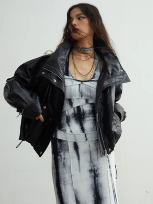 Side three-quarter view of black glossy faux leather outerwear with oversized silhouette, exposed zipper and snap buttons, styled with layered neck jewelry