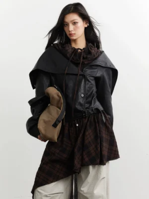 Close-up front view of a black faux leather jacket with wide lapels drawstring neckline and detachable dark tartan plaid hem panel
