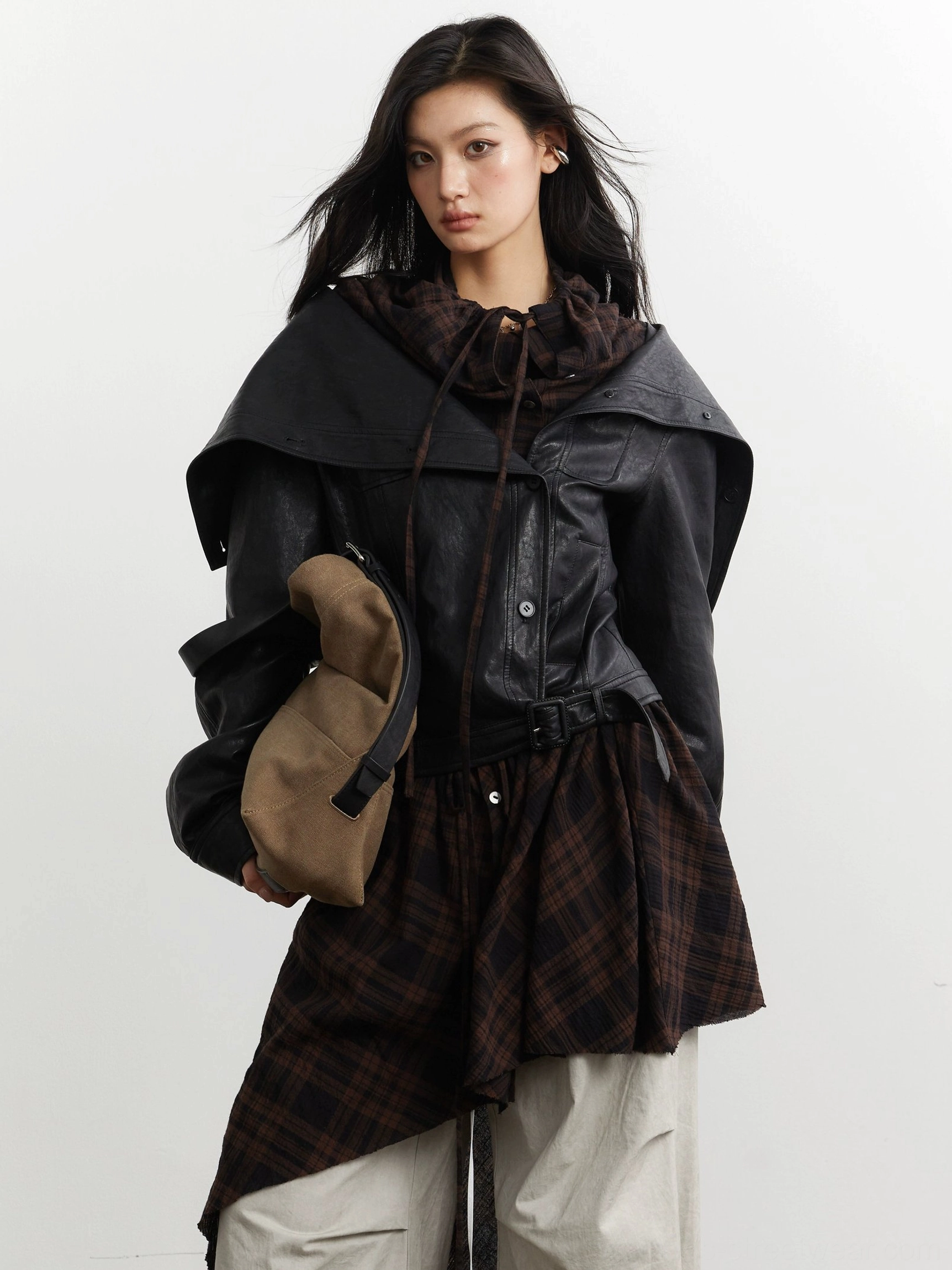 Close-up front view of a black faux leather jacket with wide lapels drawstring neckline and detachable dark tartan plaid hem panel