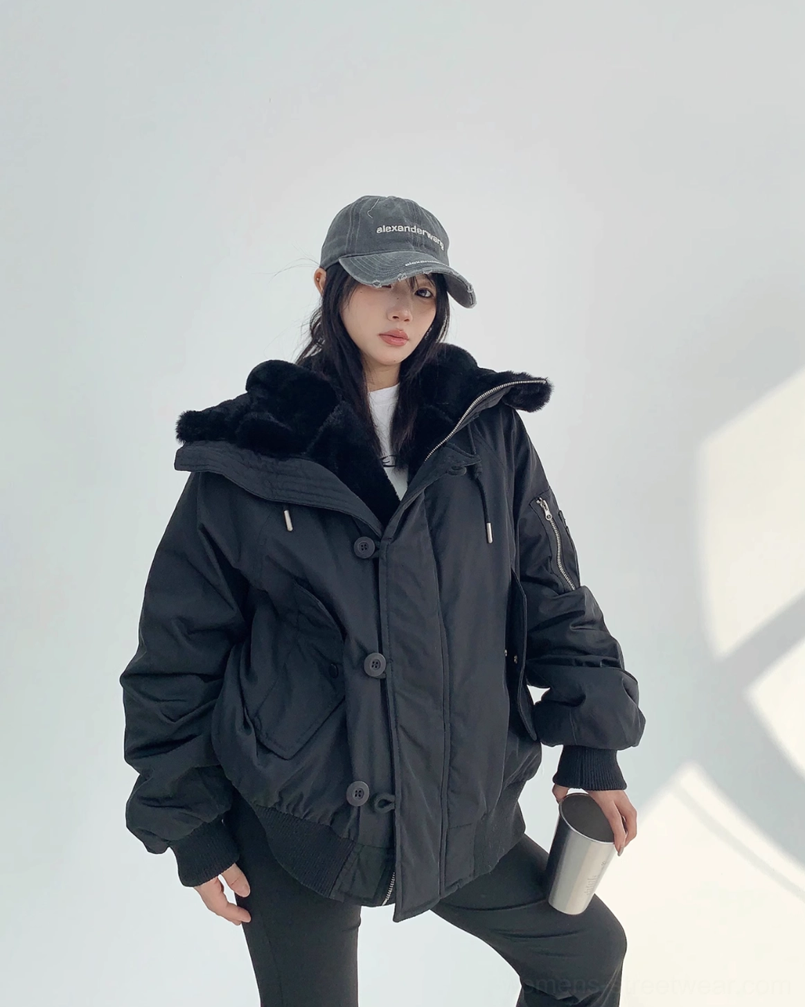 Black faux-shearling bomber jacket with an oversized hood, padded sleeves, ribbed hem, and contemporary Y2K streetwear mood