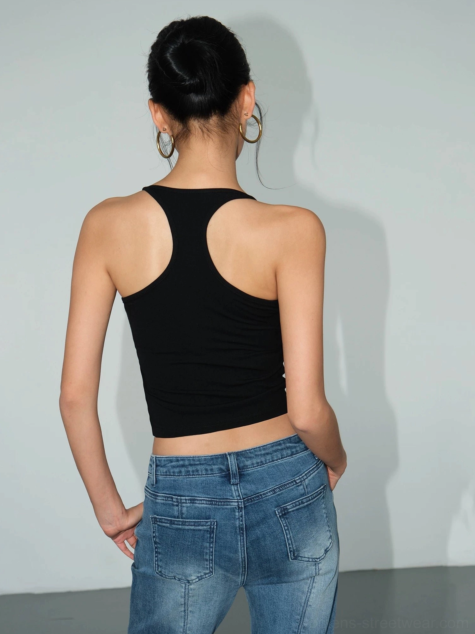 Black fitted racerback knit crop tank for women shown in a full back view with blue denim jeans