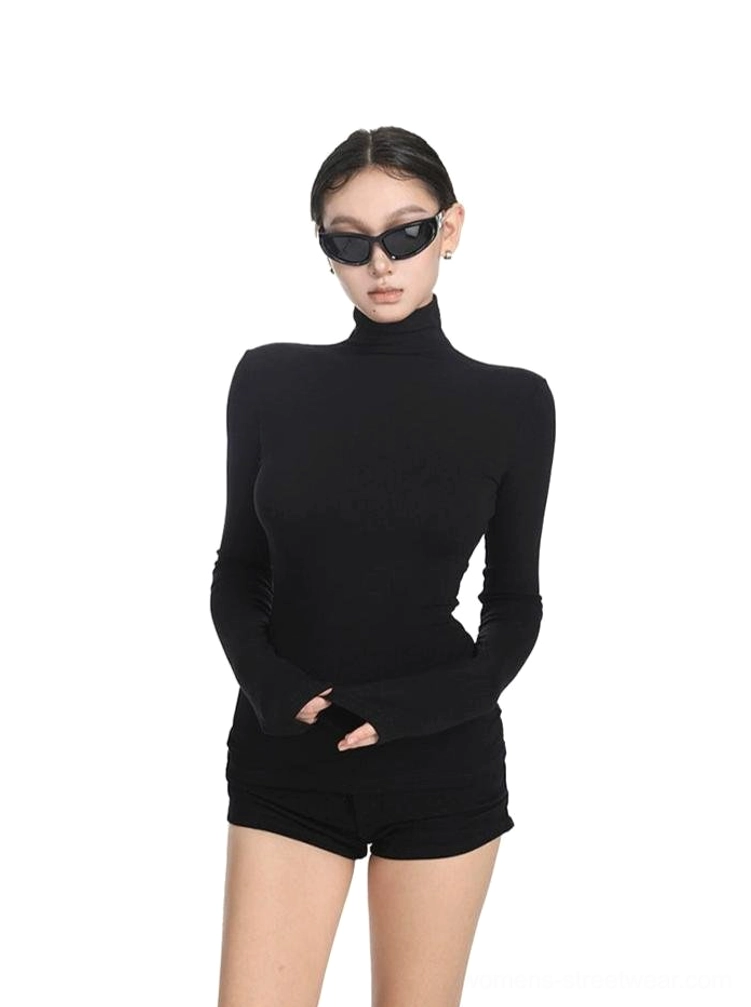 Three-quarter view of a black womens fitted turtleneck top with finger-covering extended sleeves styled in an all-black modern streetwear outfit