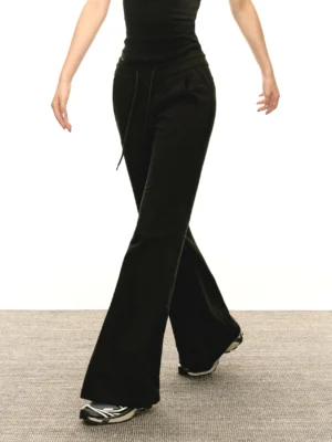 Three-quarter side view of black flared streetwear sweatpants with a slim upper-leg fit, adjustable drawstring waistband, full-length flare, cropped top, and sneakers