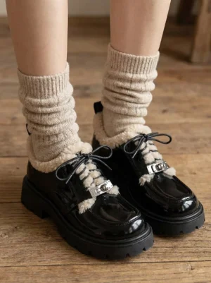 Top-down view of women's black fleece-collar platform Oxford shoes styled with beige ribbed leg warmers on a wooden floor
