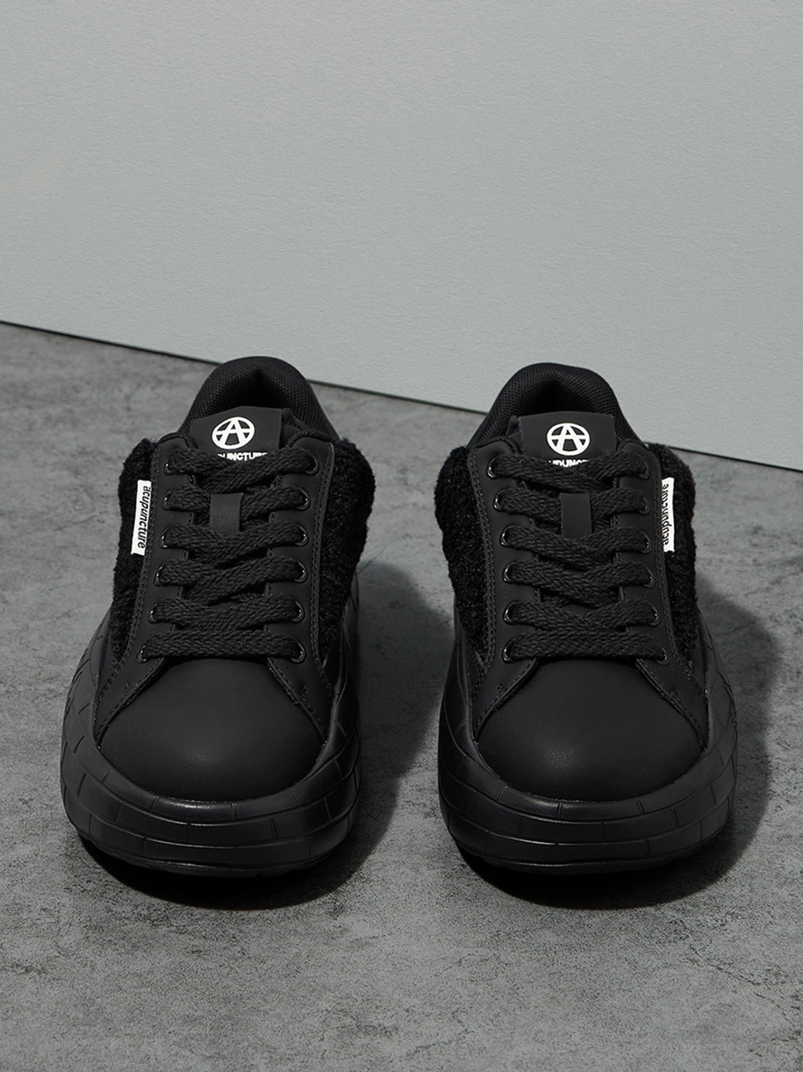 Front view of black fleece-panel platform sneakers with tonal laces, plush upper sections, and thick soles