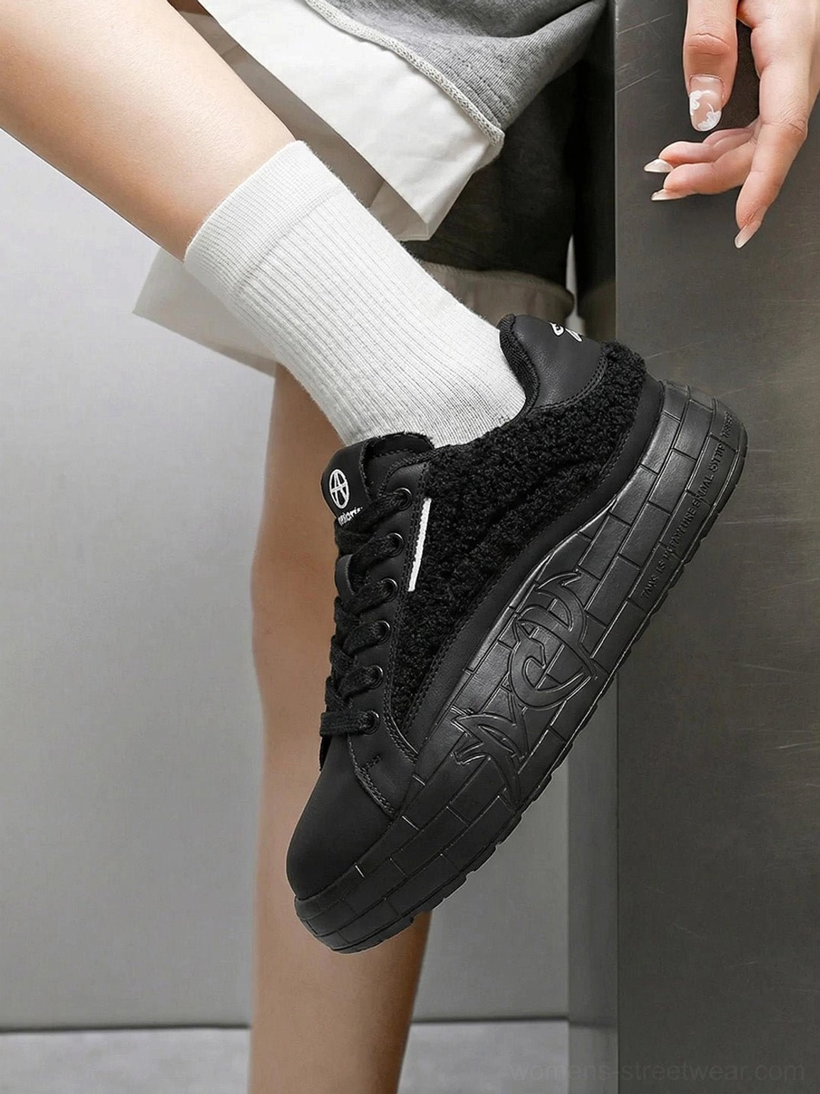Close-up of black fleece-panel sneakers worn with white crew socks and light gray casual trousers