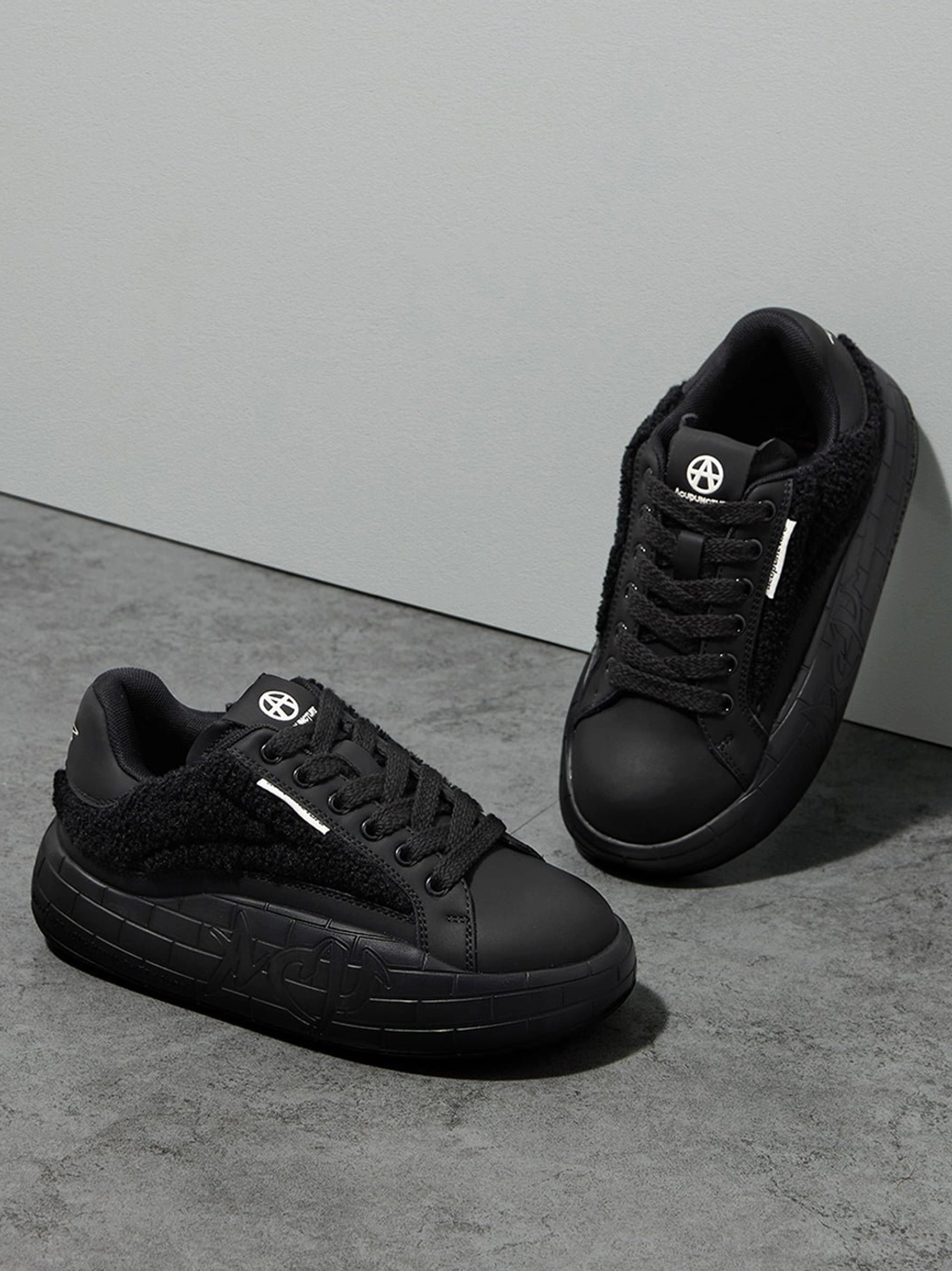 Black fleece platform sneakers shown at an angled studio view with chunky embossed soles and lace-up uppers