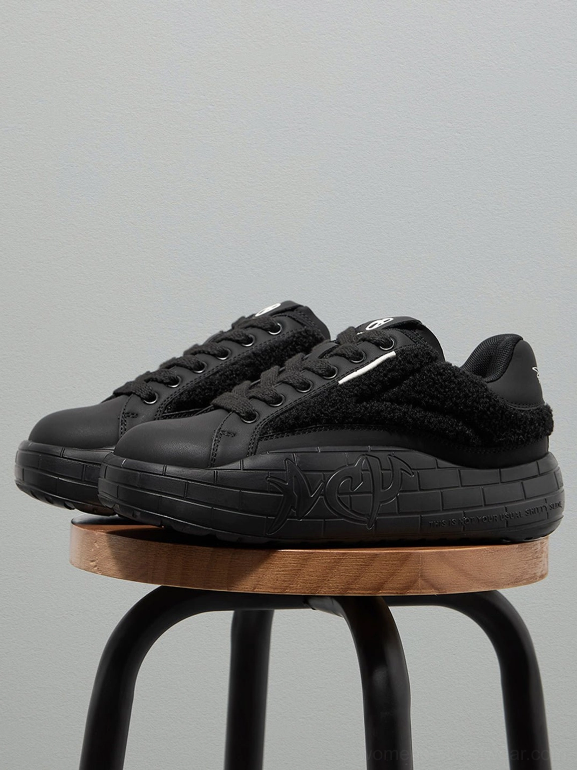 Pair of black fleece platform sneakers displayed on a wooden stool with plush panels and sculpted soles