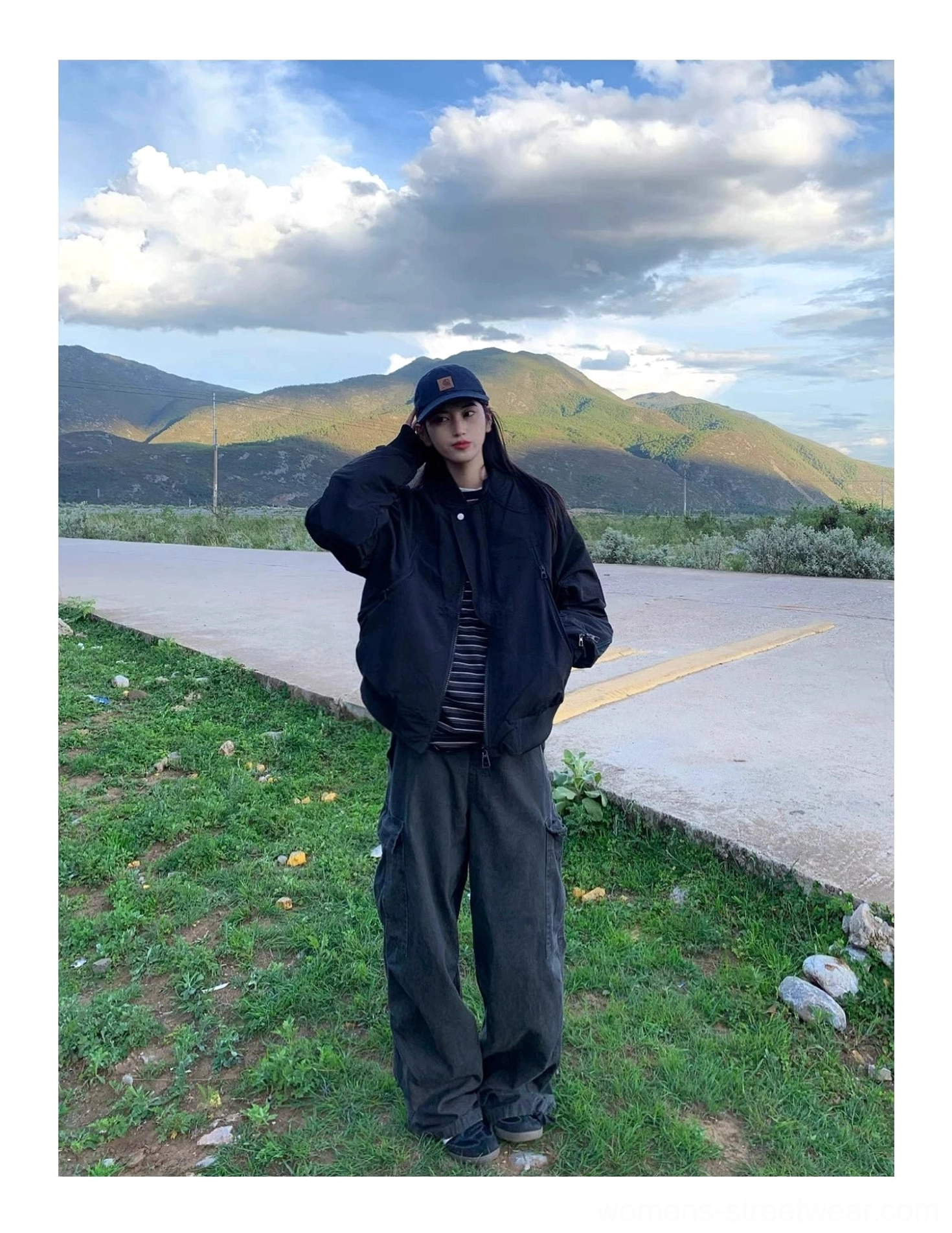 Black flight bomber jacket styled with a striped top, baseball cap, and cargo pants at sunset
