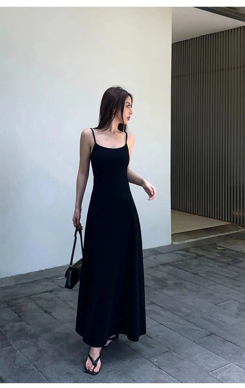 Black floor length spaghetti strap dress shown in side profile with casual black flip flops