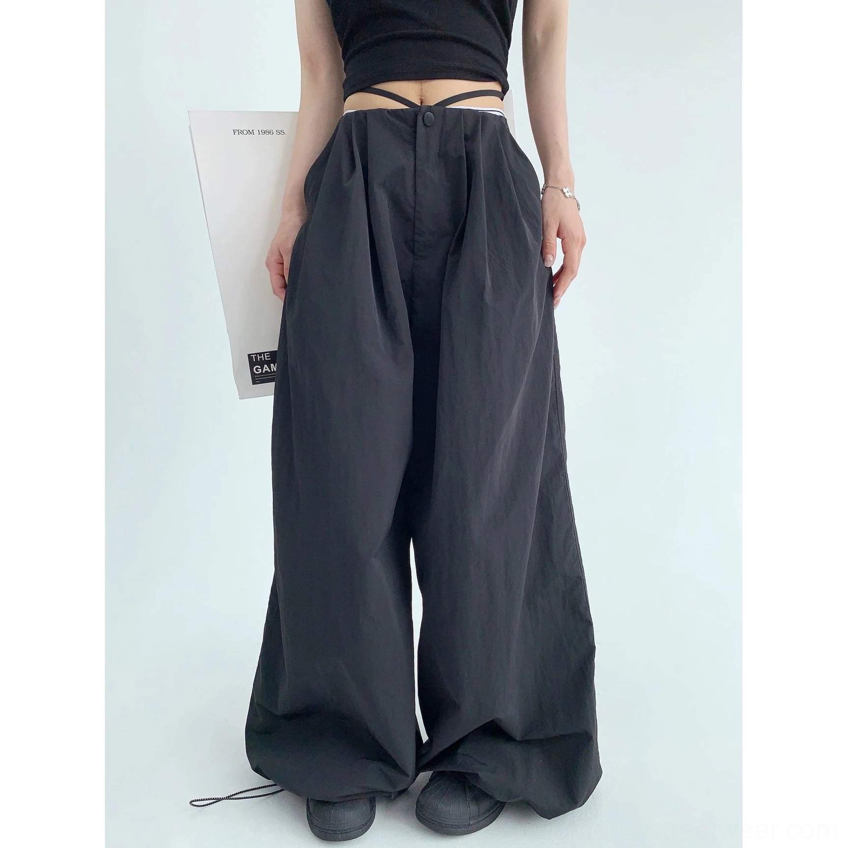 Black floor-length wide-leg parachute pants shown from the back three-quarter view with relaxed drape and exposed waist tie