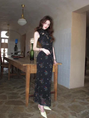 Full body side view of a black floral cheongsam maxi dress with floor-length fitted silhouette, sleeveless design, and white pointed heels