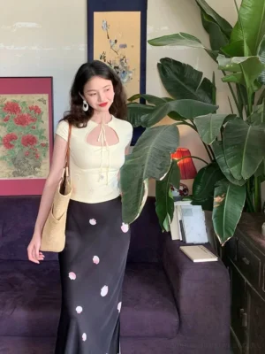 Front view of a black floral viscose maxi skirt with high waist and fishtail-inspired flare styled with a cropped top in a vintage interior