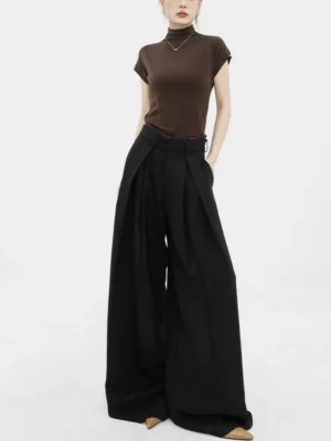 Front three-quarter view of black high-waisted fluid pleated wide-leg streetwear trousers styled with a brown fitted top