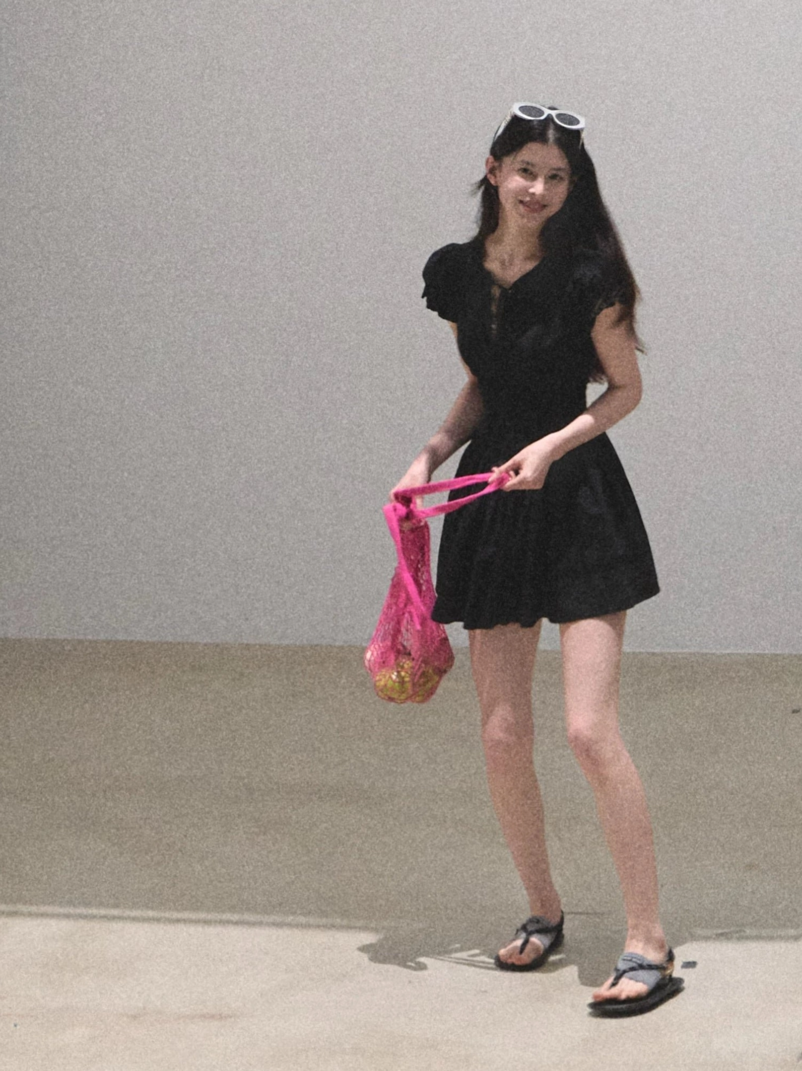 Black flutter sleeve mini dress styled with a pink mesh tote bag in a minimalist studio setting