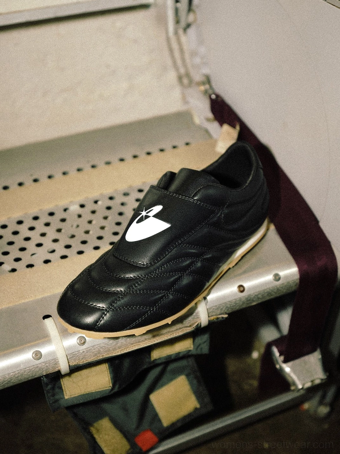 Close-up black football-inspired sneakers showing textured quilted upper, tongue patch, laces, and strap detail