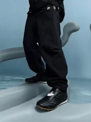 Black football-inspired trainer sneakers styled with black cargo pants in a modern indoor streetwear setting