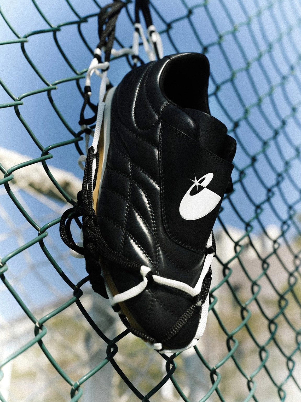 Black football trainer sneakers featuring a sleek low-cut collar, quilted vamp, adjustable strap, and gum outsole