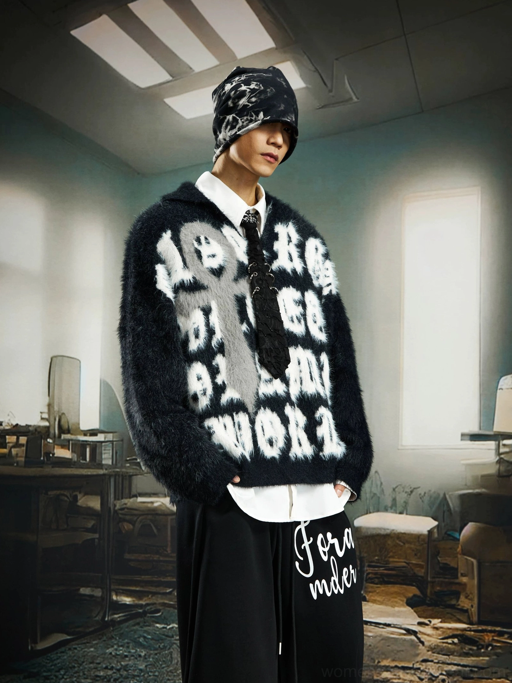 Three quarter front view of a black fuzzy jacquard sweater with gothic lettering and cross graphic in an avant garde streetwear outfit