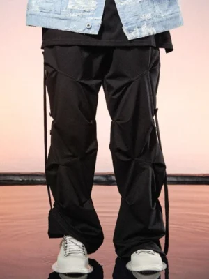 Black geo-sculpt wide-leg streetwear cargo pants styled with a denim jacket and white sneakers in a sunset waterside streetwear setting