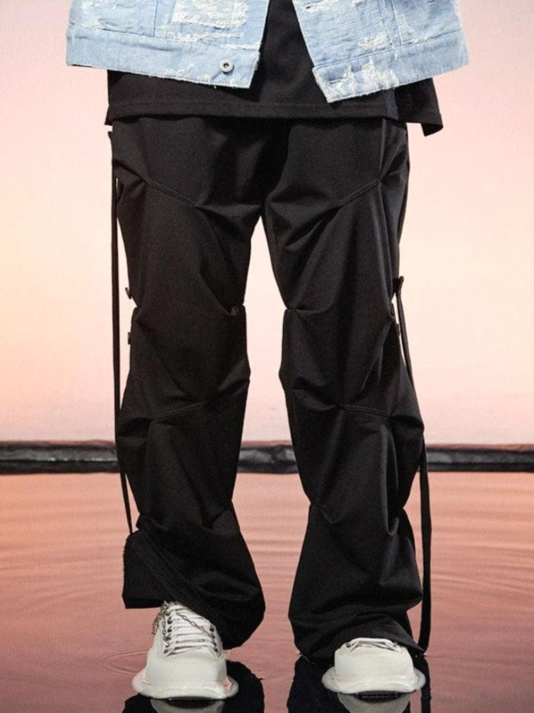 Black geo-sculpt wide-leg streetwear cargo pants styled with a denim jacket and white sneakers in a sunset waterside streetwear setting