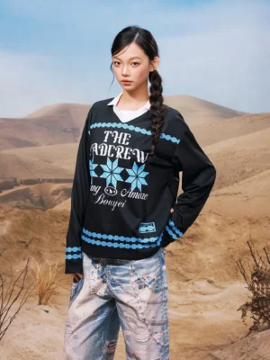 Black oversized geometric graphic collared long sleeve streetwear shirt shown from the front three-quarter view with blue folk-inspired snowflake prints and distressed jeans