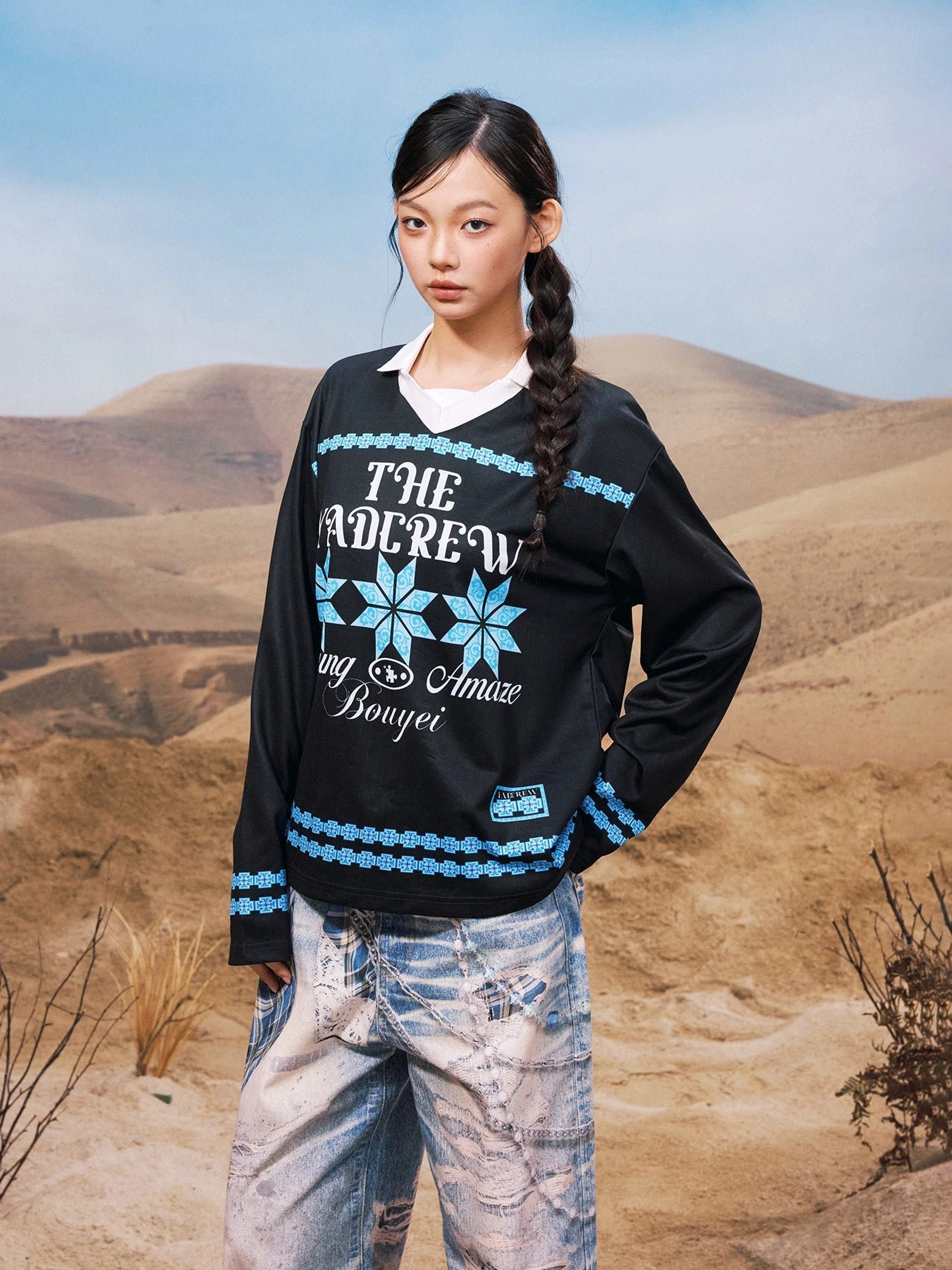 Black oversized geometric graphic collared long sleeve streetwear shirt shown from the front three-quarter view with blue folk-inspired snowflake prints and distressed jeans